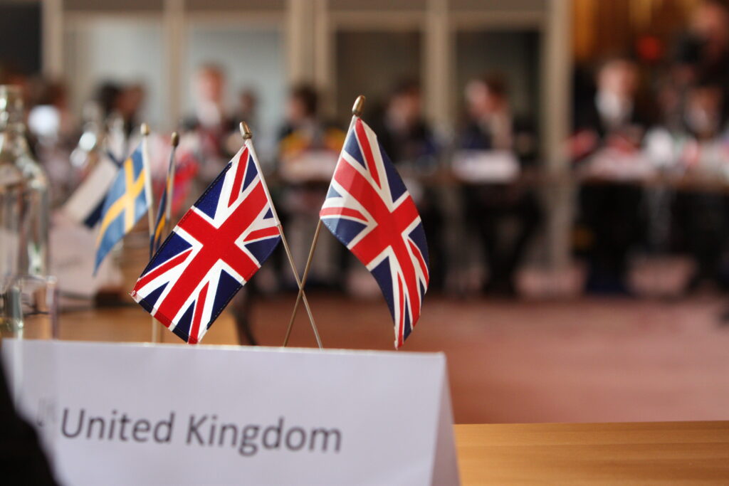 Two Union flags on a table behind a United Kingdom sign.