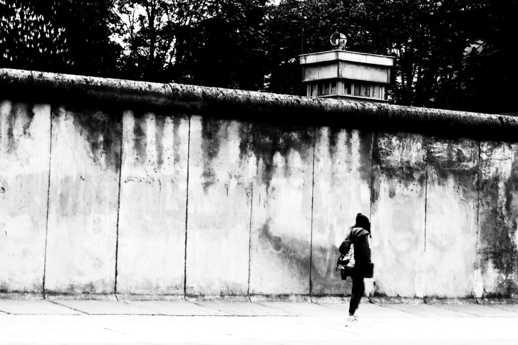 Black and white image of a section of the Berlin Wall on a street with pedestrian walking past